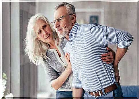 An older woman holds up an older man, who grabs his back