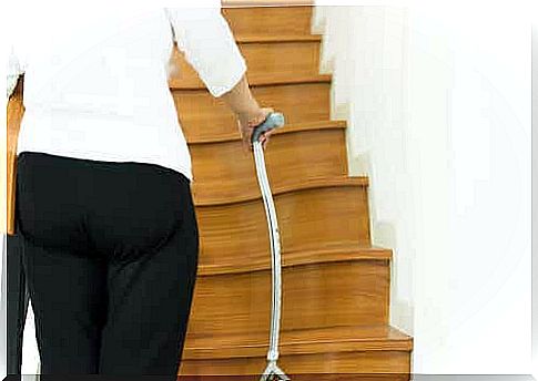 An elderly woman uses a cane to walk up the stairs